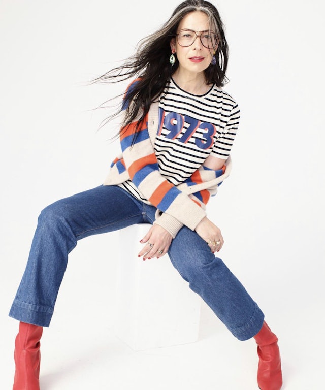 Model wearing The Modern 1973 Tee in cream/navy stripe with blue jeans a cardigan,and red boots