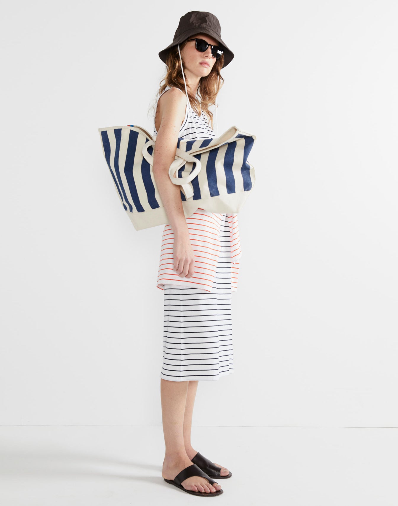 Model wearing The Tank Dress - White/Navy Pinstripe while holding The Over The Shoulder All Over Striped Tote - Canvas/Navy